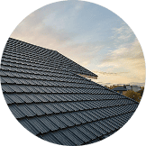 A close-up view of a tiled roof by Pantheon Roofing in Florida, with a partly cloudy sky and buildings visible in the background.