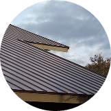 A metal roof with overlapping sections by Pantheon Roofing, set against a cloudy Florida sky and a partial view of trees.