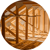 Exposed wooden roof trusses and beams inside an unfinished attic, with sunlight filtering through the structure—showcasing the craftsmanship typical of Pantheon Roofing in Florida.