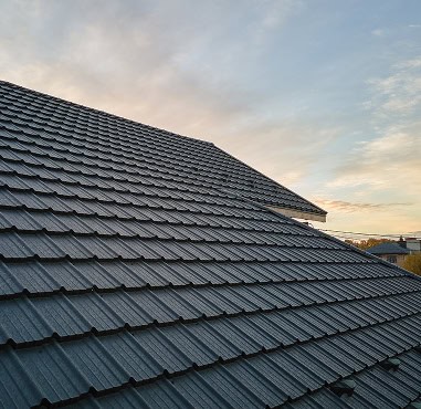 A close-up view of a sloped roof with gray shingles by Pantheon Roofing, photographed at sunset under a partly cloudy Florida sky.
