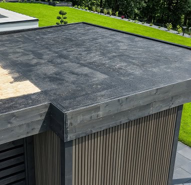 Flat black roof by Pantheon Roofing on a modern Florida building with partially unfinished shingles, surrounded by green lawn and landscaping.