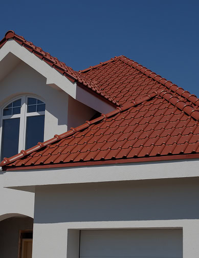 A house with a white exterior and a red tiled pantheon roofing, featuring arched windows, sits under the clear blue Florida sky.