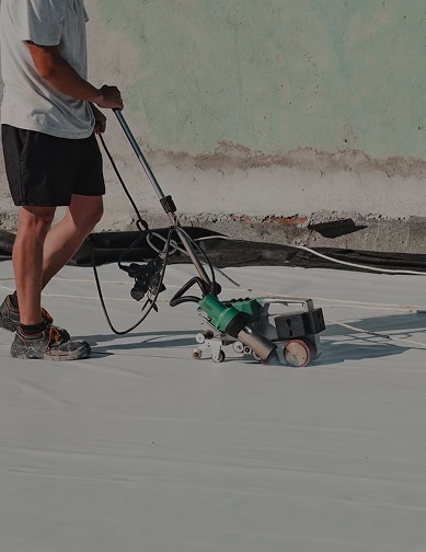 A person from Pantheon Roofing in Florida operates a machine to apply or seal a white material on a flat surface, likely for roofing or flooring work.