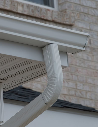 Close-up of a white metal rain gutter and downspout attached to the roof edge of a brick house, showcasing quality installation by Pantheon Roofing in Florida.