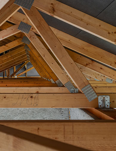 Wooden roof trusses with metal plates and connectors in an unfinished building attic, showcasing the quality framework typical of Pantheon Roofing projects in Florida.