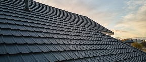 Close-up view of a sloped roof covered with dark gray shingles by Pantheon Roofing, with part of a chimney visible and Florida’s cloudy sky in the background.