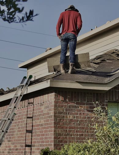 A person in a red shirt and jeans stands on a house roof with scattered shingles, next to a ladder leaning against the brick wall—perhaps assessing repairs for Pantheon Roofing in sunny Florida.